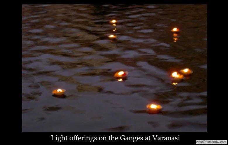Multiple small floating lights on the Ganges River at Varanasi during dusk or evening.