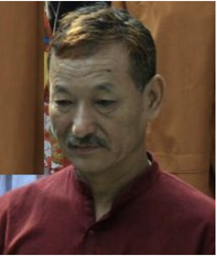 A man with short brown hair and a mustache, wearing a maroon shirt, standing indoors.