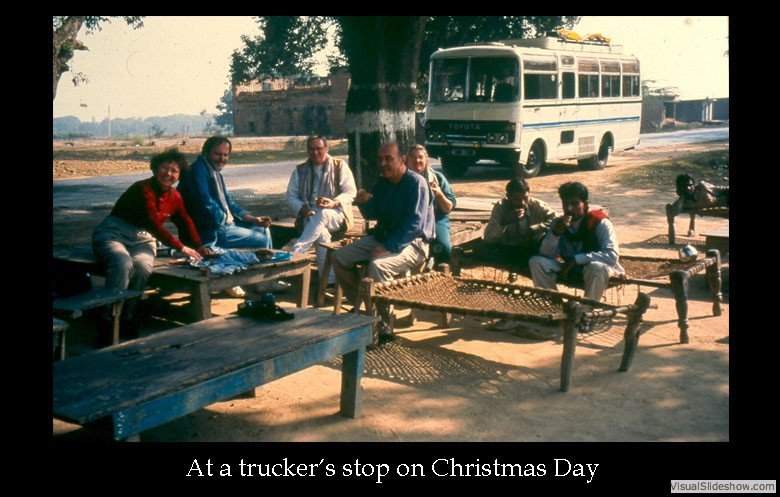 Group of people sitting outdoors at a truck stop on Christmas Day, with a bus visible in the background.