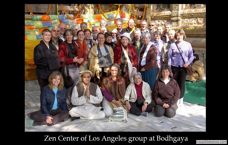 Group of diverse people at Bodhgaya, some seated and some standing, with colorful decorations and temple architecture in the background, representing the Zen Center of Los Angeles.