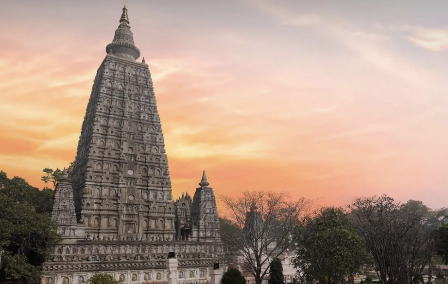 A historic temple with intricate architectural details during a colorful sunset with trees in the foreground.