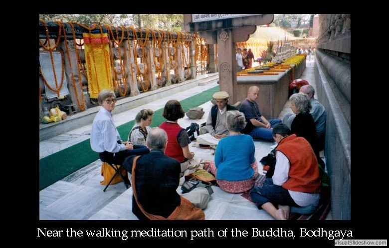 People sitting in a circle meditating near the walking meditation path of Buddha at Bodhgaya, India, with prayer flags and offerings in the background.