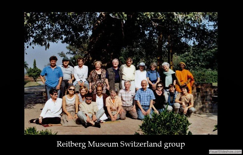 Group of people posing outdoors under a large tree, with a mix of men and women smiling, in casual attire. Caption reads 'Reitberg Museum Switzerland group.'