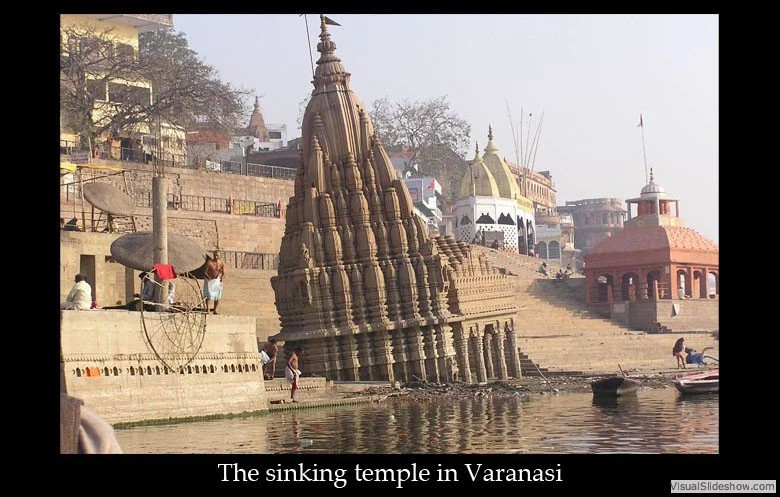 The image shows a temple partially submerged in water, giving the appearance of sinking, with people on the steps and nearby structures around the water in Varanasi.