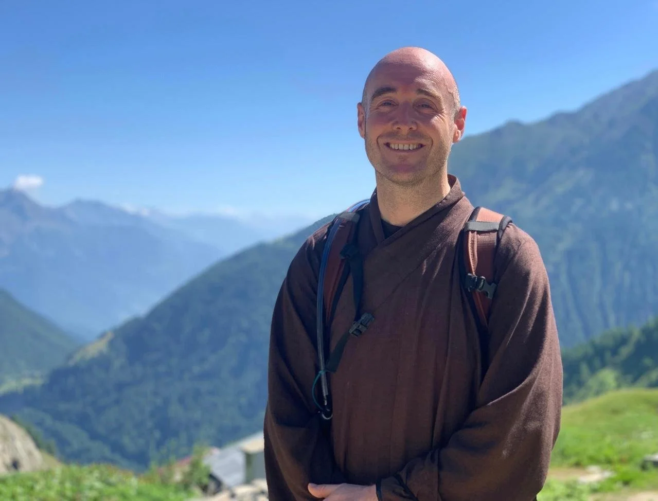 Close-up of smiling middle-aged man with gray hair and beard against a pink background.