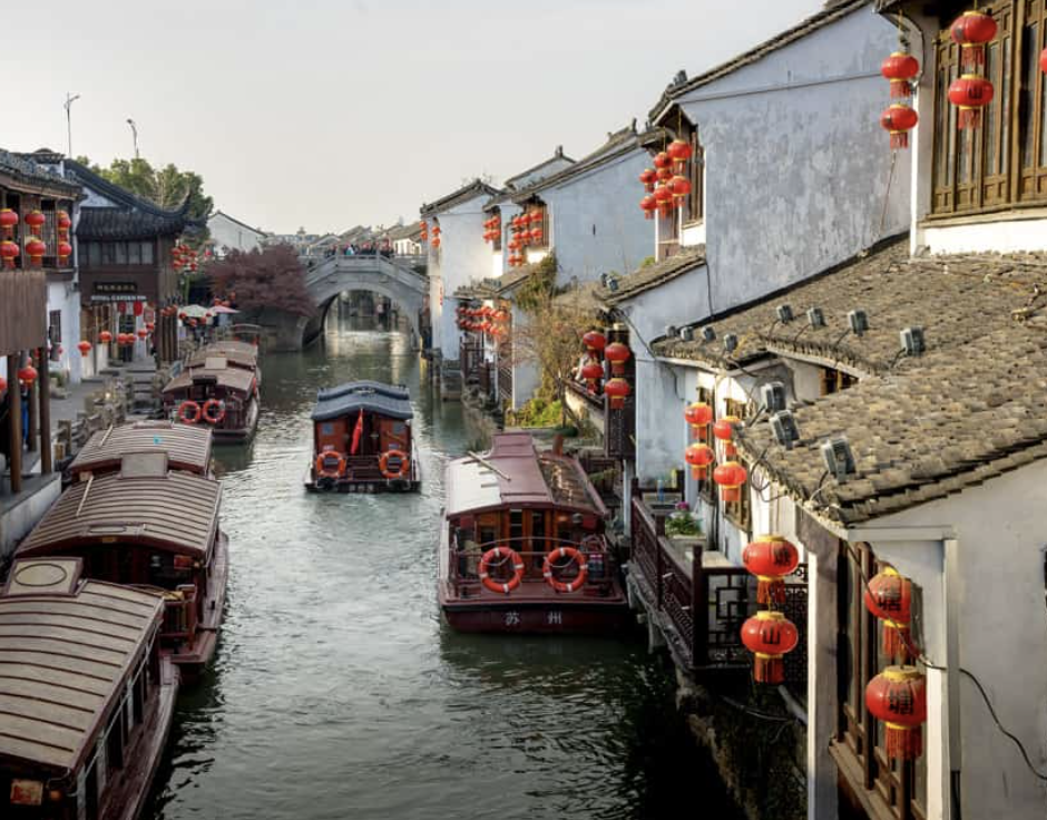 View of a riverside with boats, old buildings, and temples in the background during sunset.