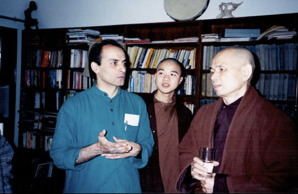 Three people in conversation in a room with shelves of books and a satellite dish on top of a bookshelf.