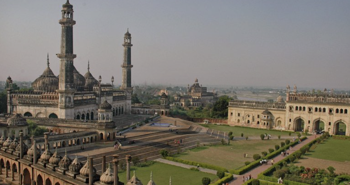 A historic palace with domes and minarets, surrounded by well-maintained gardens and pathways, in a cityscape view.