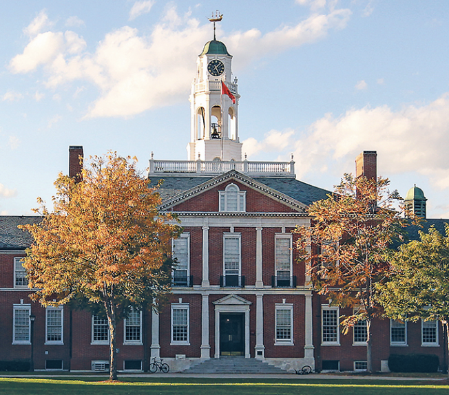 Front view of a historic brick building with a clock tower, surrounded by autumn-colored trees.