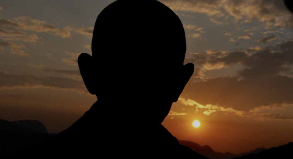 Silhouette of a person with shaved head watching a sunset with a partly cloudy sky.