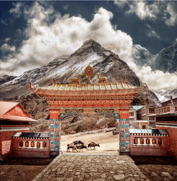 A colorful traditional Asian gate with ornate decorations, set against a mountainous landscape with snowy peaks and clouds.