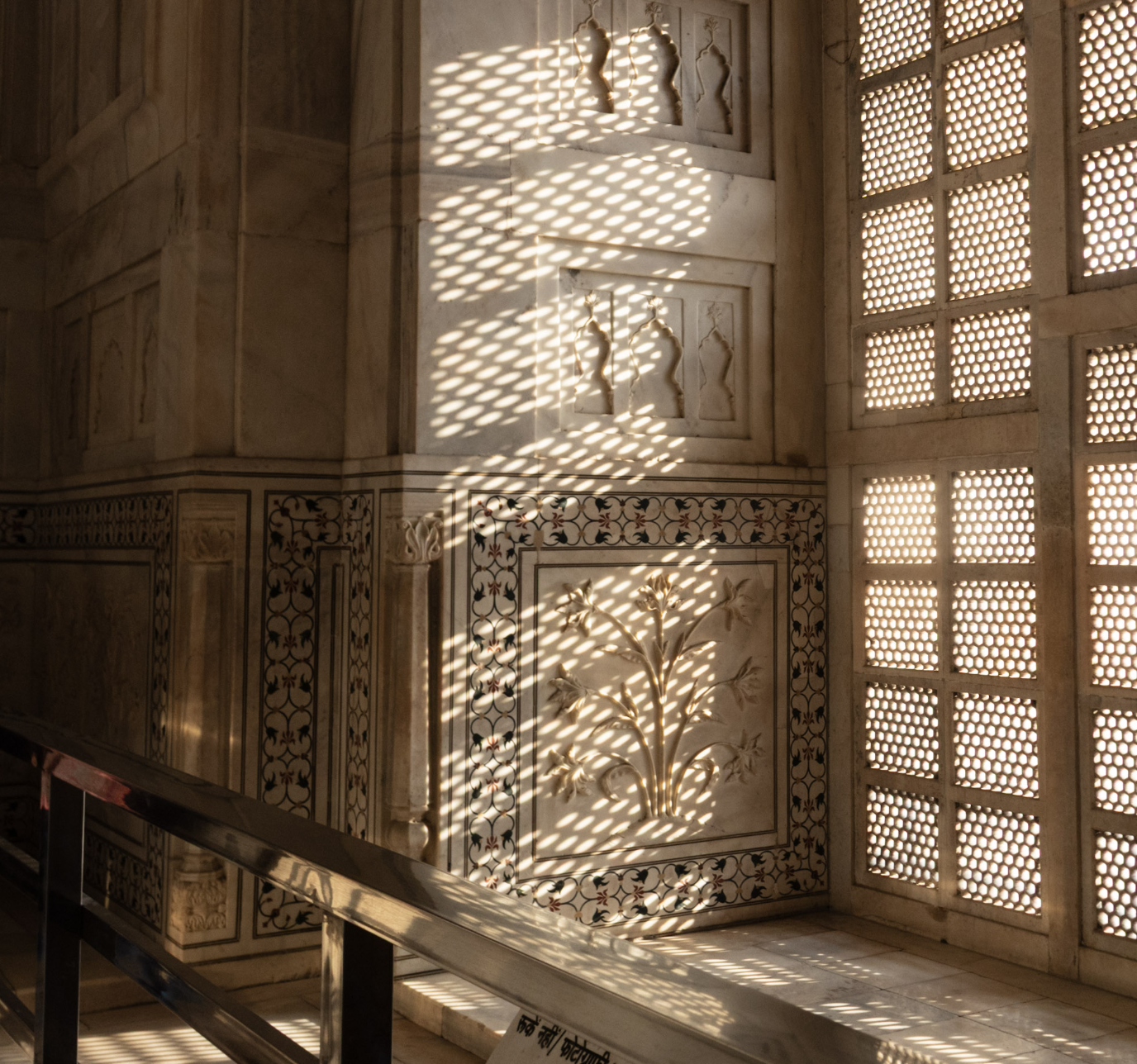 Sunlight passing through decorative lattice holes creates intricate shadow patterns on marble walls and artwork.