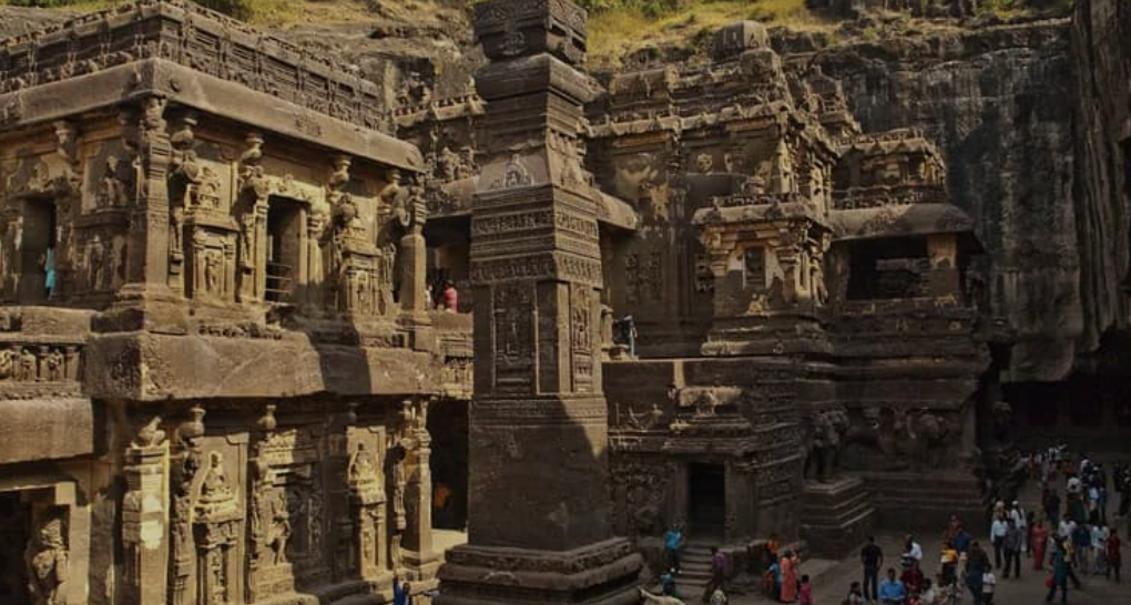 Ancient Indian rock-cut cave temples with intricate carvings and statues, bustling with visitors.