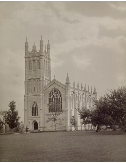 Black and white photo of a Gothic-style cathedral with tall towers, large stained glass windows, and surrounding trees in a park.