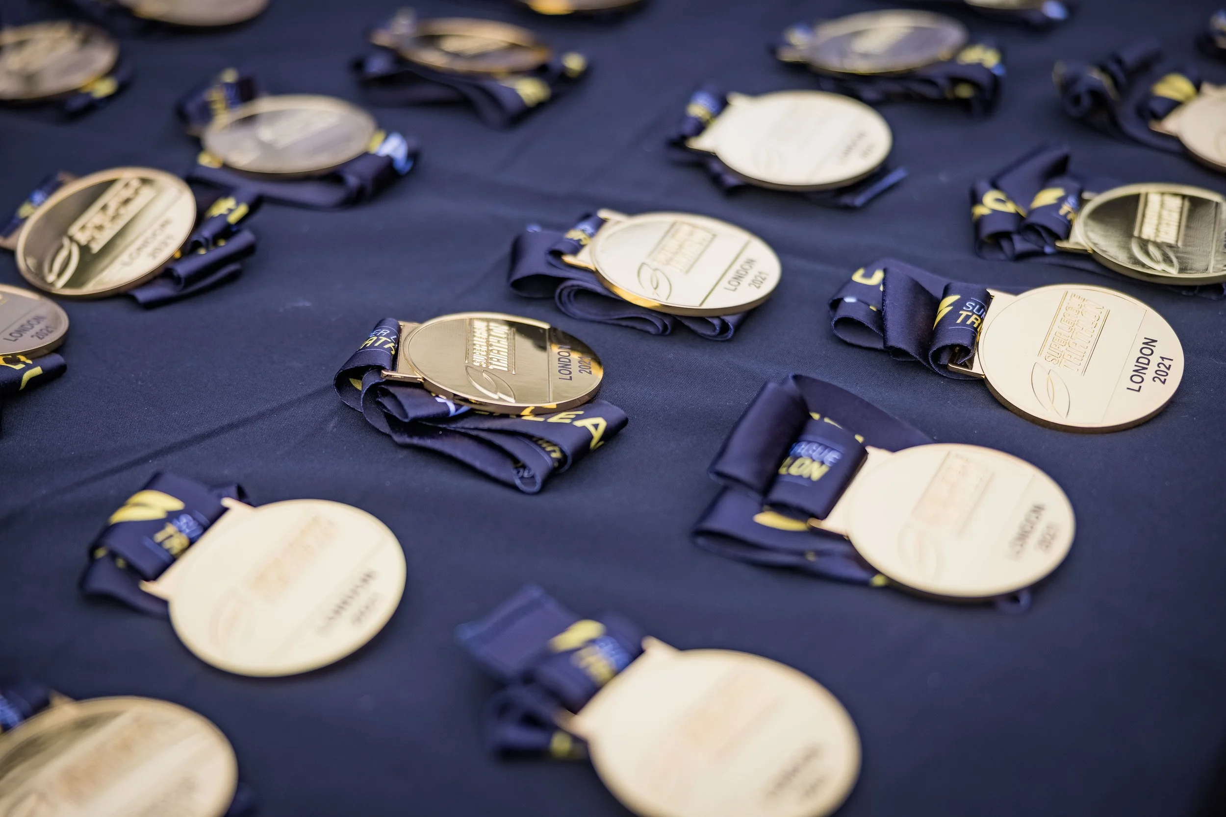 Multiple gold medals with blue ribbons arranged on a dark surface, likely for an awards ceremony or competition.