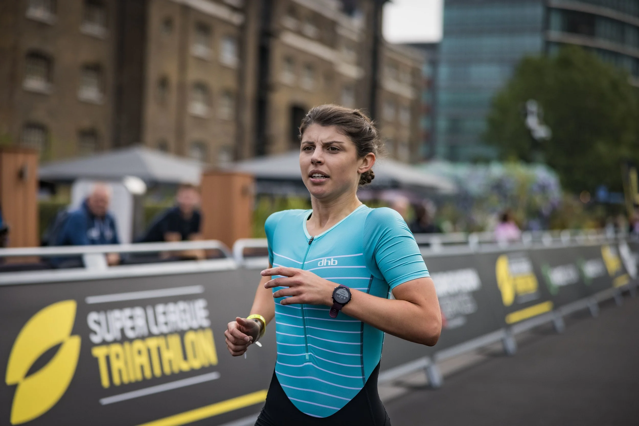 Female athlete running during a triathlon race in an urban setting with buildings and spectators in the background.