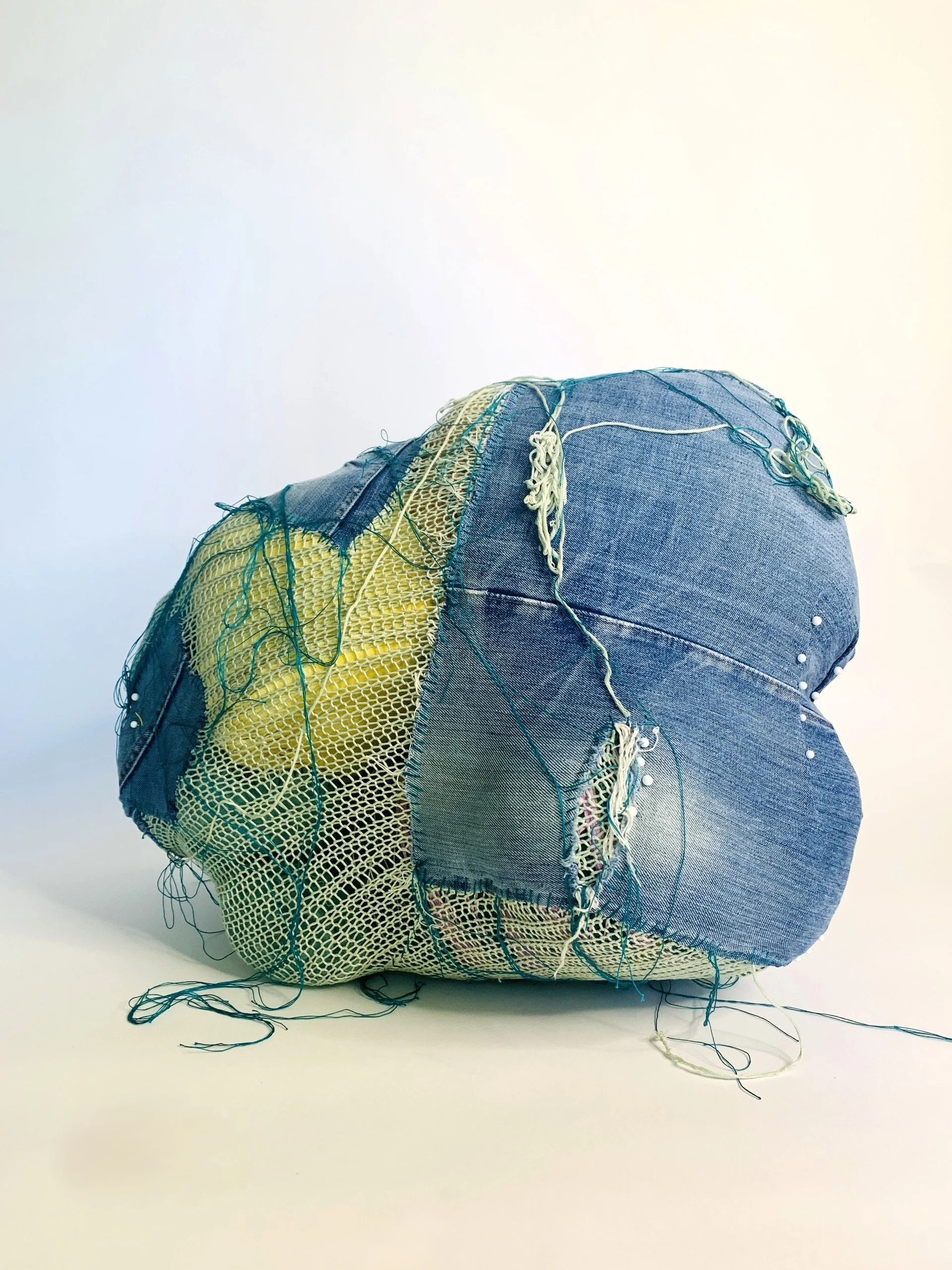  Kristina de Coninck 
 Harsh waters
 Sections of mattress, hand-knitted top
in a pale green dye, denim, textile and
cotton threads
 45 × 60 × 40 cm
 2025