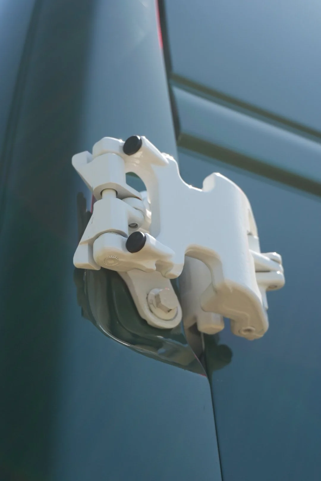 Close-up of a white latch and hinge mechanism attached to a teal vehicle door.
