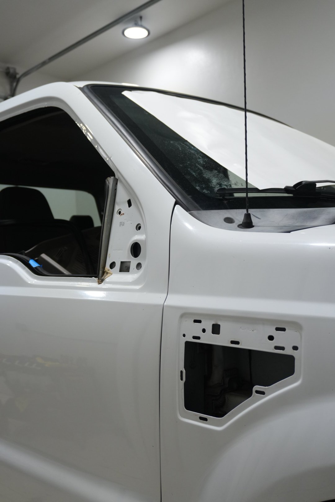 Partial view of a white pickup truck with the front side panel and driver side mirror removed, showing internal mounting holes and open space where parts are missing.