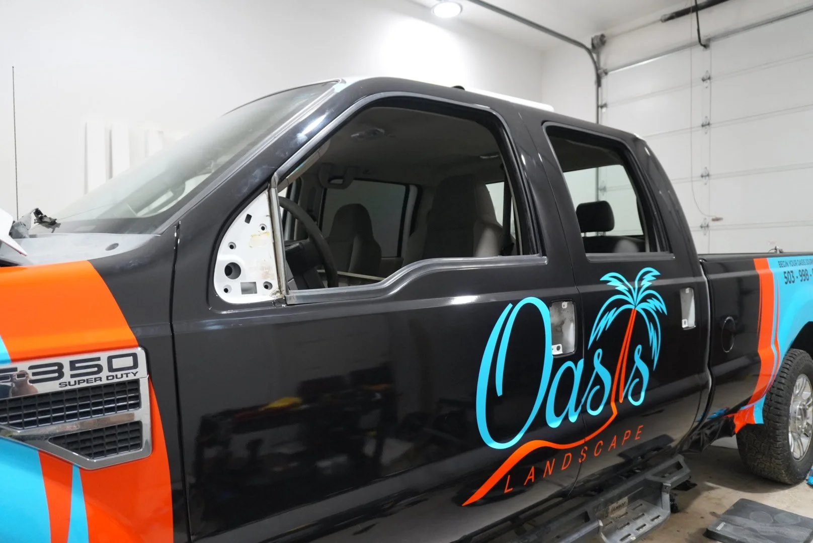 Black pickup truck with Dentil logo and tropical palm tree graphic, partially disassembled, inside a garage.