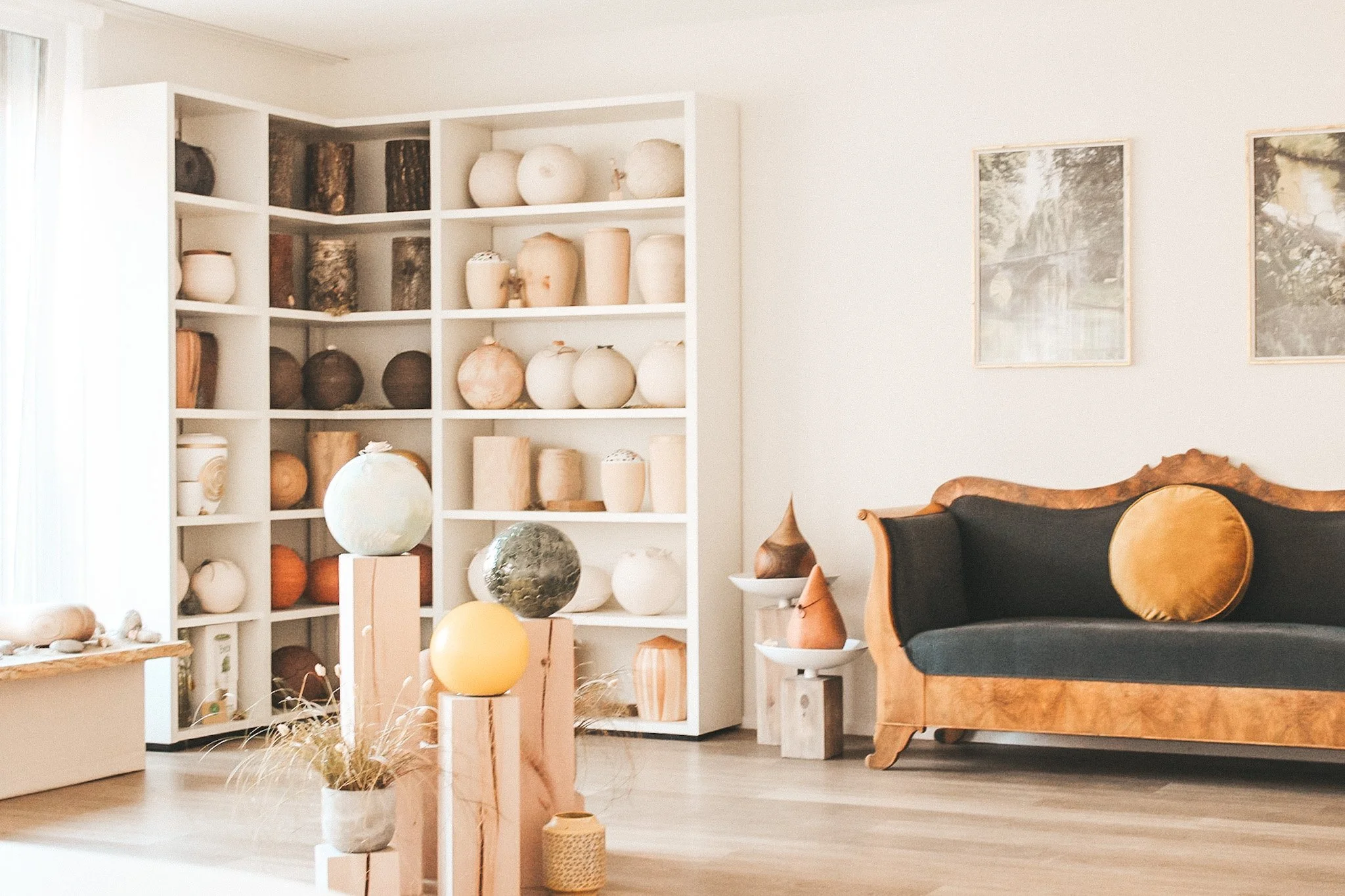 Stilvoll eingerichteter Beratungsraum mit handgefertigten Urnen in neutralen Tönen, präsentiert in einem offenen Regal. Die warme Atmosphäre wird durch ein antikes Sofa und natürliche Materialien unterstrichen – ideal für persönliche Bestattungsgespr