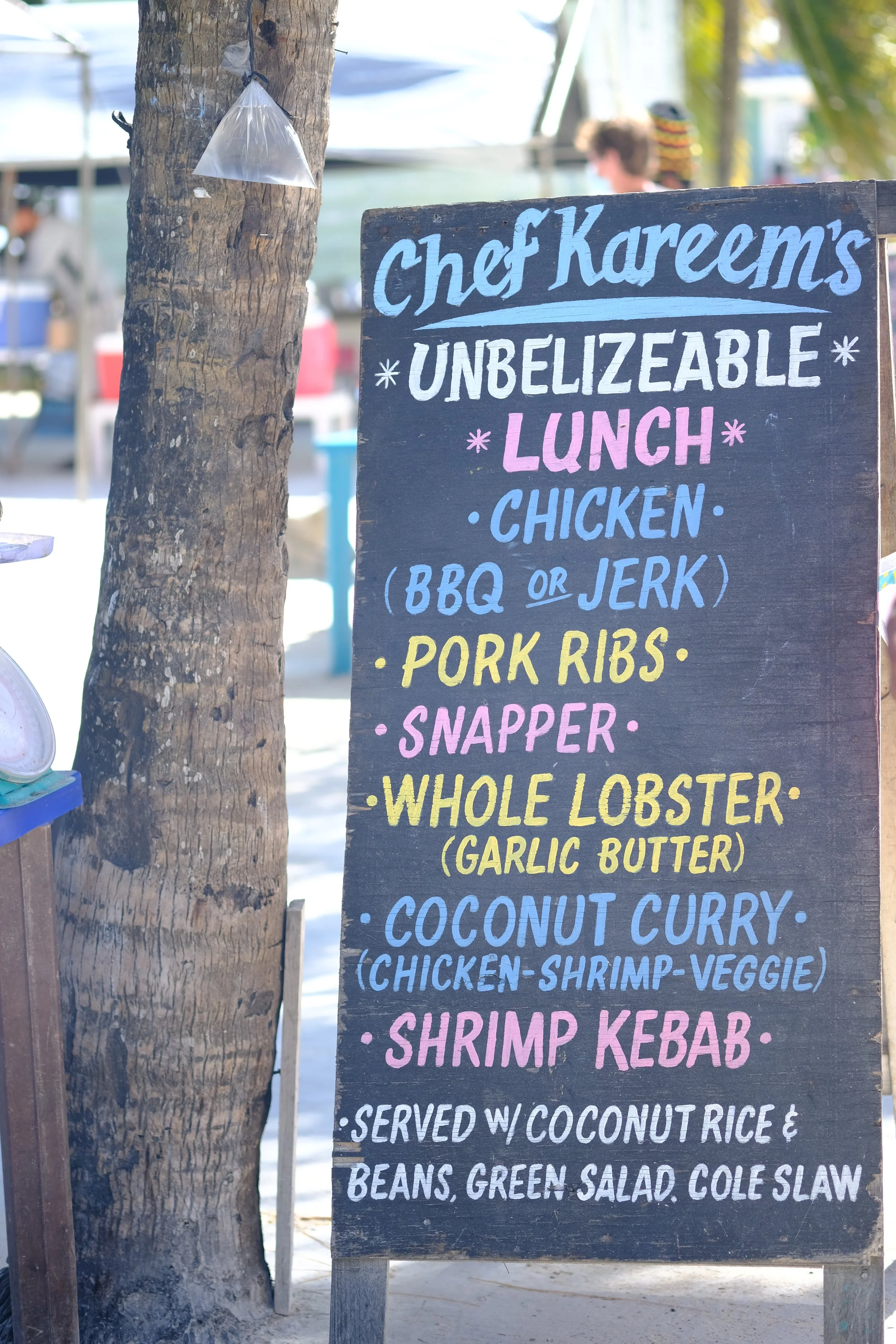 A blackboard menu listing lunch options at a food stand, including chicken, pork ribs, shrimp, and coconut curry dishes, with colorful handwritten text.