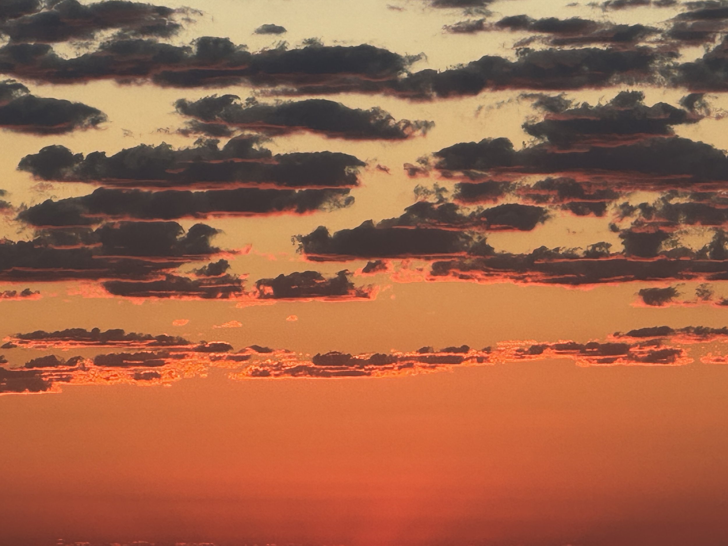 A vibrant sunset sky with scattered dark clouds and reddish-orange hues near the horizon.