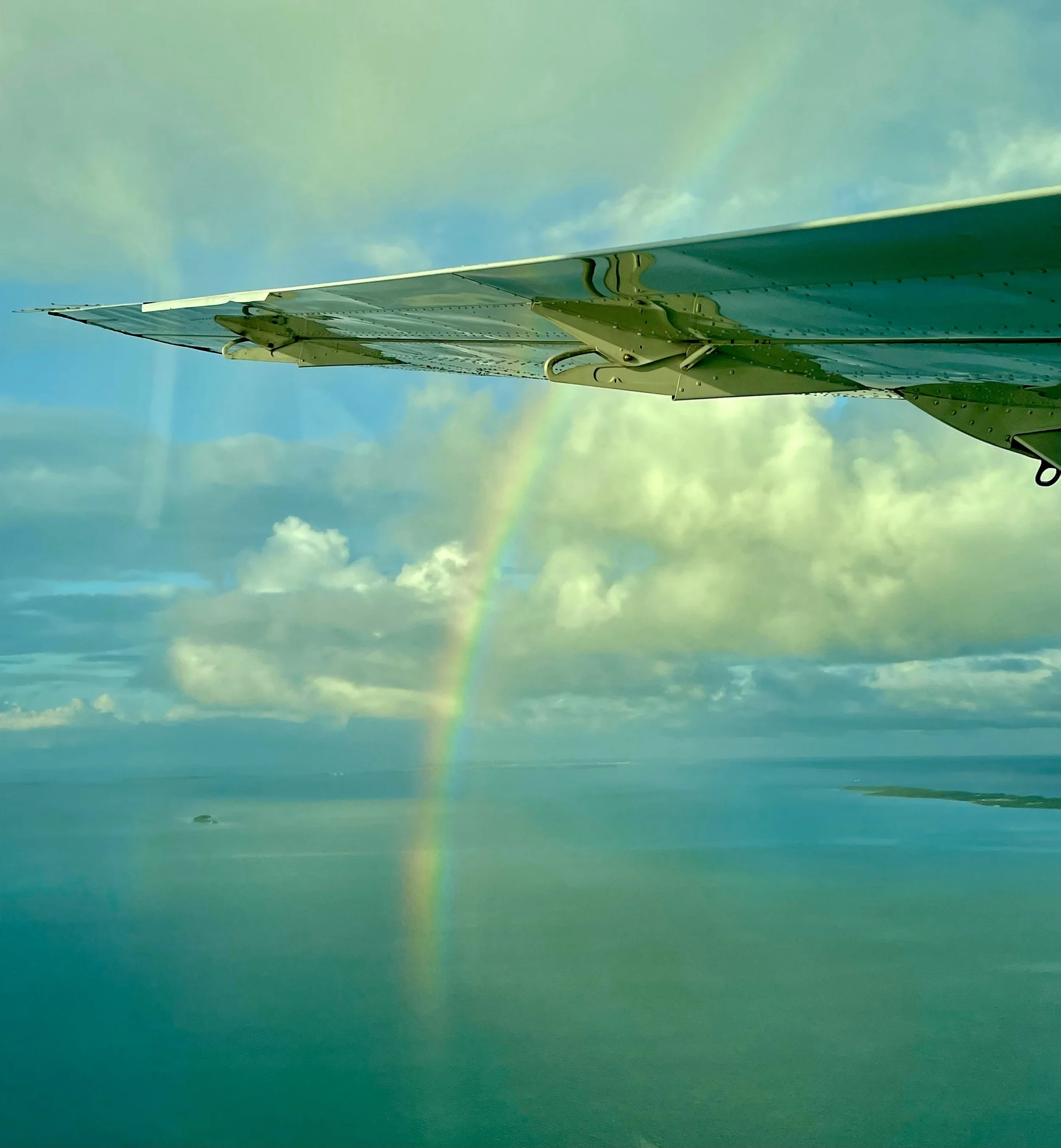 Colorful rainbow appears over the ocean with a partly cloudy sky in the background.