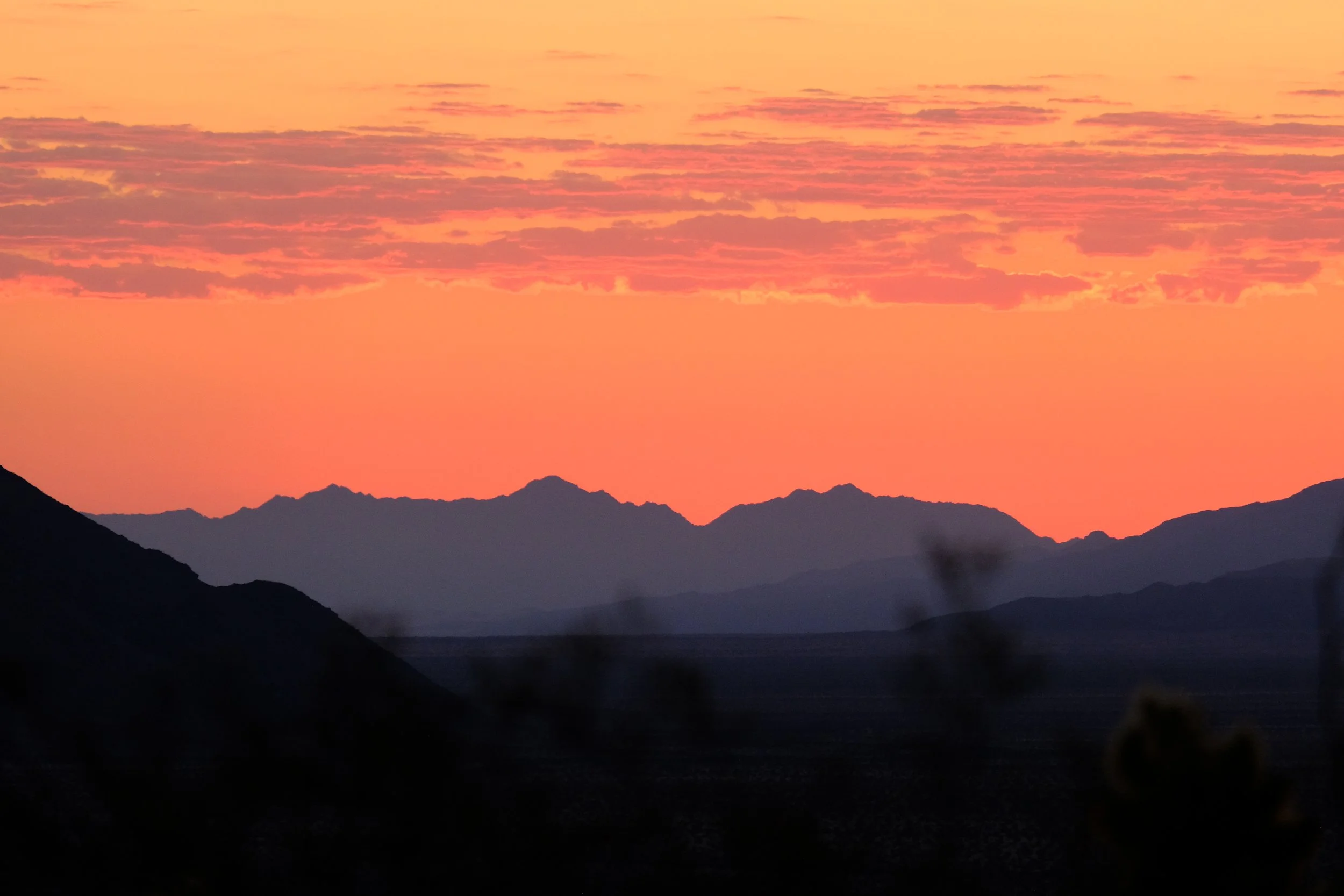 A sunset with orange and pink clouds over a silhouette of mountain ranges.