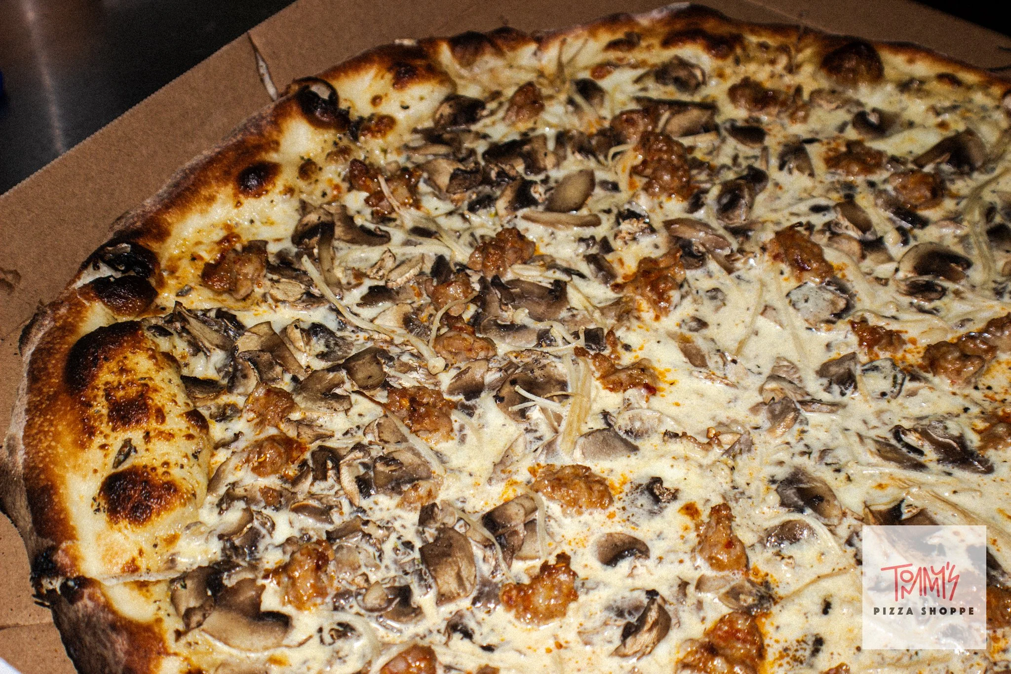 A close-up of a sliced mushroom and sausage pizza in a cardboard pizza box.