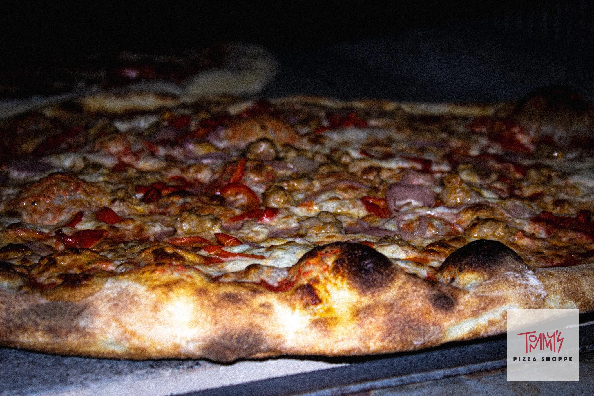 New York-style pizza baking in a deck oven at Tommy's Pizza Shoppe in Guam, topped with pepperoni, Italian sausage, mushrooms, onions, and roasted red peppers.