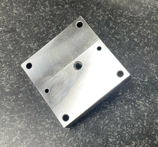 A silver metal block with multiple holes, placed on a dark surface.