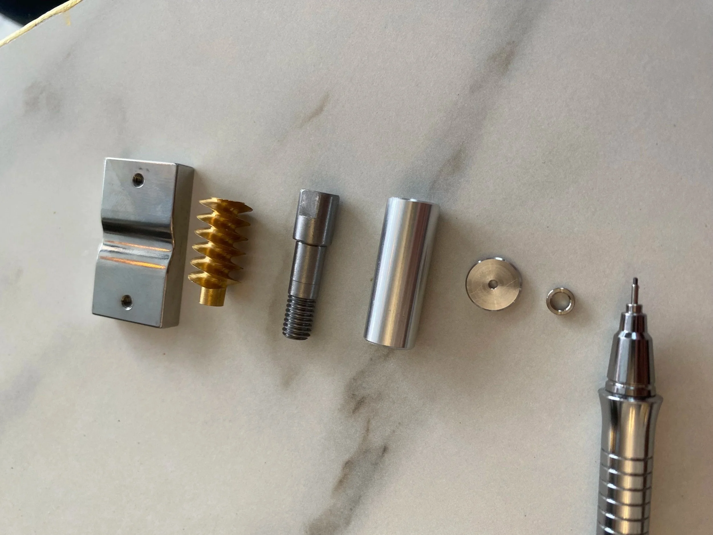 Disassembled mechanical pen with various metal parts on a light-colored surface.