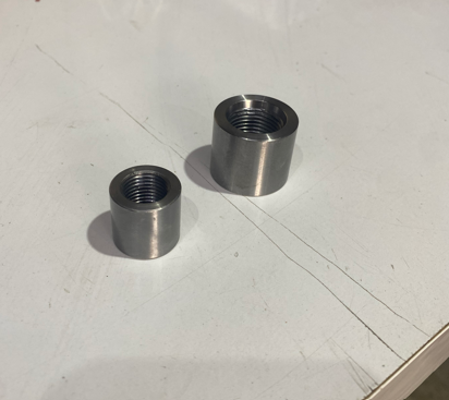 Two metallic threaded inserts or spacers on a white surface.