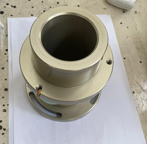 A metallic cylindrical mechanical part with a hollow center placed on a white sheet of paper.