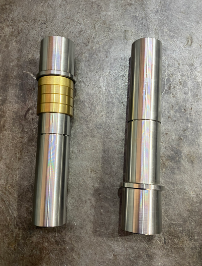 Two metal cylindrical objects lying on a gray surface, with one having gold-colored rings.