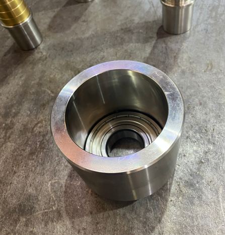 A cylindrical metal component with a hollow center, placed on a workbench or table.