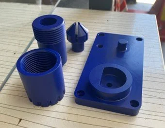 Three blue plastic electrical or plumbing components with a cylindrical shape, a cap, and a rectangular base with a raised circular protrusion, all placed on a wooden surface.
