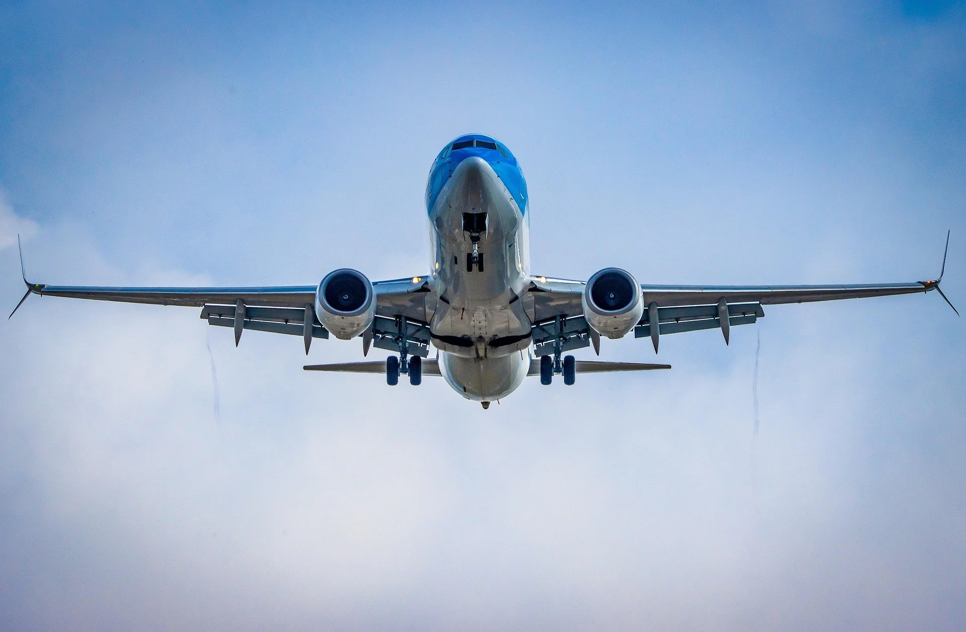 A commercial airplane flying low against a cloudy sky, viewed from below.