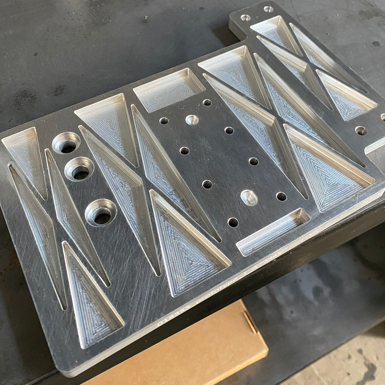 Metal machined component with multiple drilled and beveled holes and triangular cutouts.