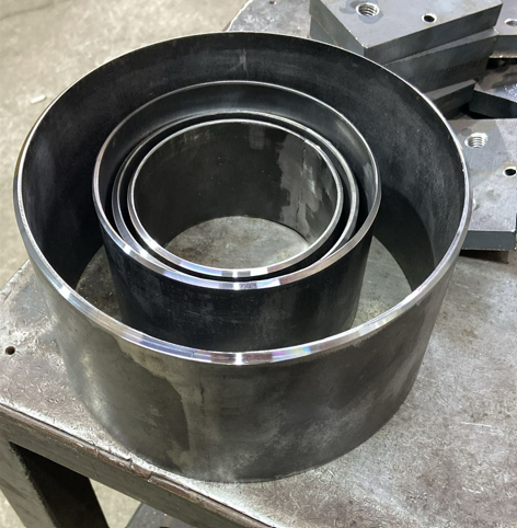 Large black metal ring with smaller fitting rings inside, on a workbench in a workshop.