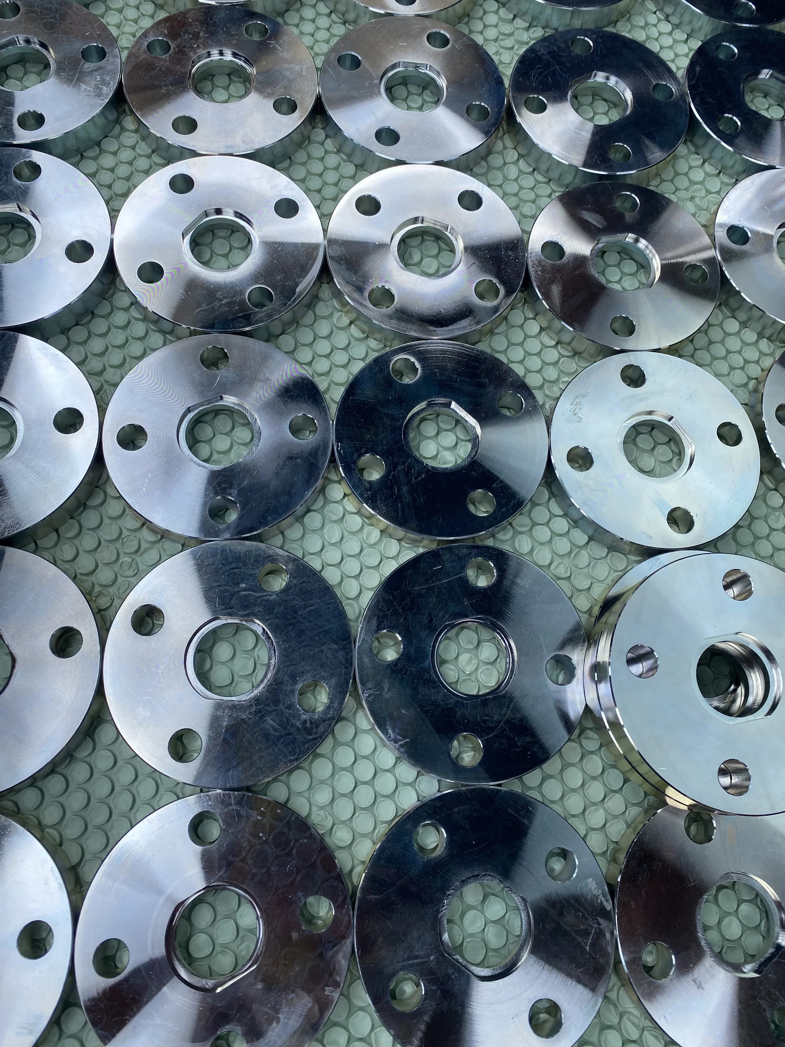 Multiple shiny metal circular components with holes, arranged on a textured green surface.
