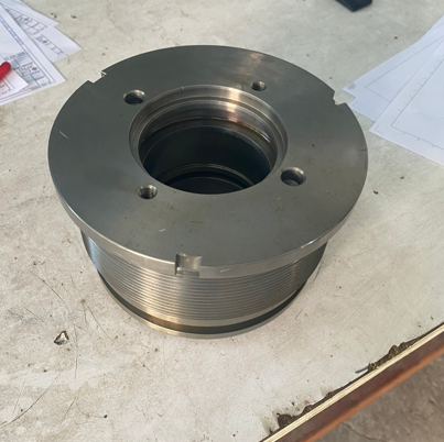 A large, metallic, circular mechanical component with a central hole and multiple bolt holes, placed on a workbench surrounded by papers.