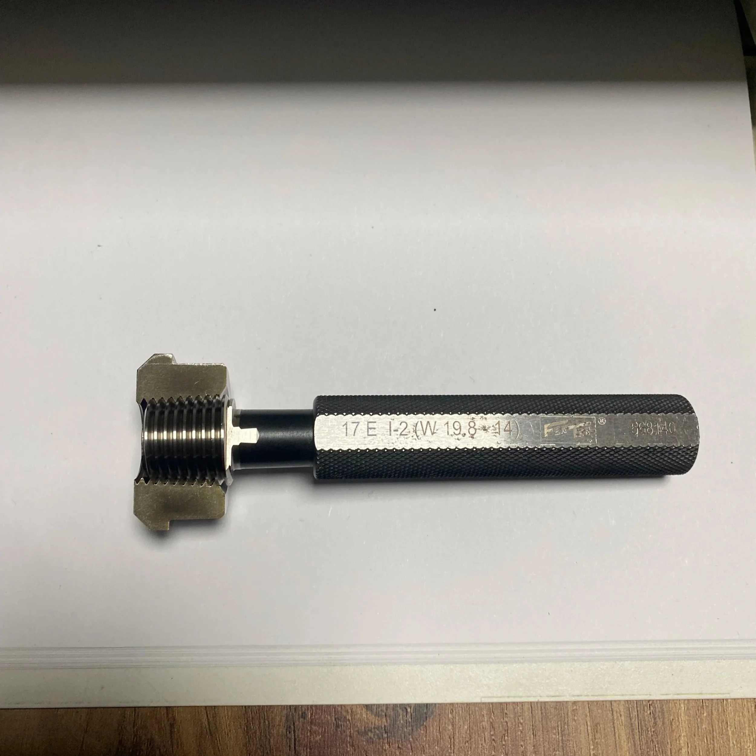 A metal tool with a textured black handle and a threaded, cone-shaped metal head placed on a white surface.