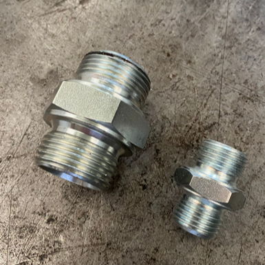 Two metal threaded pipe fittings on a rough surface, larger and smaller sizes.