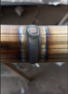 Close-up of a welded metal pipe showing colorful heat-affected zones with visible weld bead in the center.