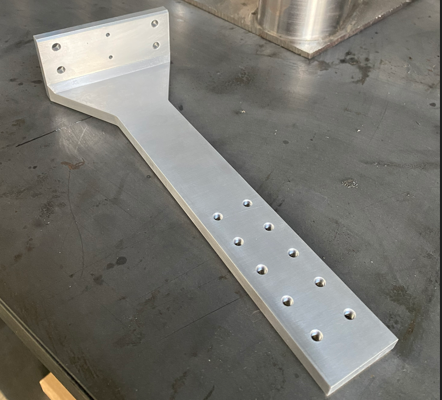 Metal L-bracket with multiple drilled holes on a dark work surface.