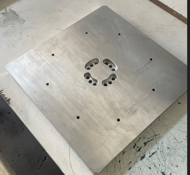A large square stainless steel industrial plate with multiple holes and a circular cutout in the center.