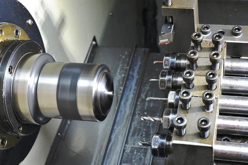 Close-up of a CNC machine turning a metal workpiece with precision, with various drill bits and fasteners visible.