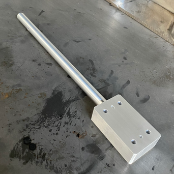 A metal bar with a rectangular attachment on one end, placed on a dark, stained surface.